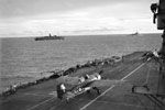 After landing a Grumman Martlet of 888 Squadron, Fleet Air Arm is seen taxi-ing along the flight deck of HMS Formidable to the forward hangar. HMS Warspite and the AMC Alaunia can be seen in the background during operations round Madagascar. The force left Colombo on April 24, 1942 and put into the Seychelles on May 1. The Fleet Air Arm carried out extensive searches and patrols over a wide area during the operation. The covering force then put into Mombasa on May 10 after the operation was concluded. Photo: Lt. D. C. Ouids. Imperial War Museums A 9716