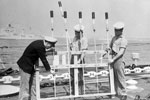PO Leslie Hirst of Scarborough, Yorkshire with AB's Fred Bidgood of Nuneaton, and Ronald White of Hornecastle, Lincolnshire, preparing rockets on HMS Sheffield for the Review fireworks display. HMS Superb is in the background. Imperial War Museums A32582